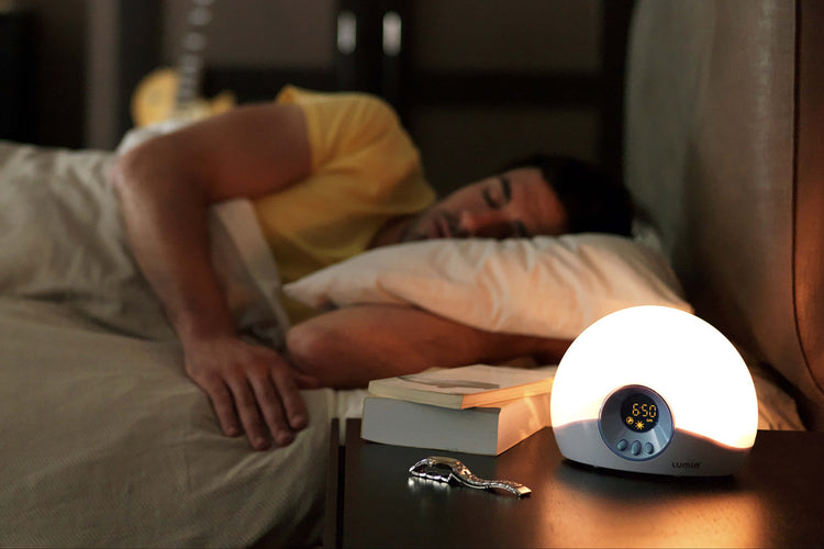 Person lying in bed with a Lumie wake-up light on a nightstand