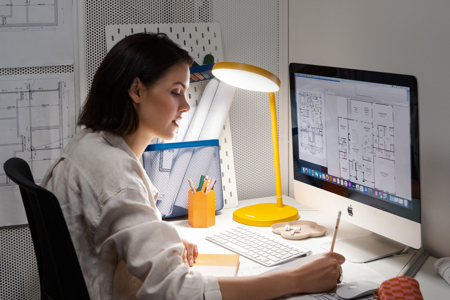 Person working at a desk with two computer monitors and a Lumie bright light therapy lamp.